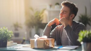 man sitting contemplating a wrapped gift and open notepad