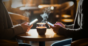 two adults at a coffee shop exchange phone numbers or text each other