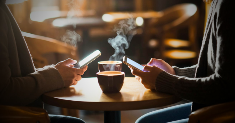 two adults at a coffee shop exchange phone numbers or text each other